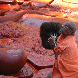 Jain monk at the feet of the vermilion annointed statue of Lord Bahubali, India